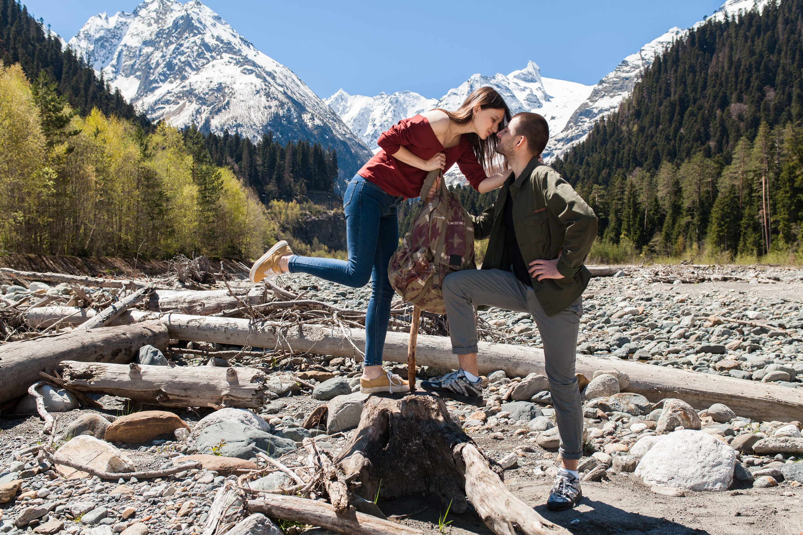 young hipster beautiful couple hiking at river in forest, jeans, sneakers, smiling, having fun, traveling, romantic vacation, mountains background